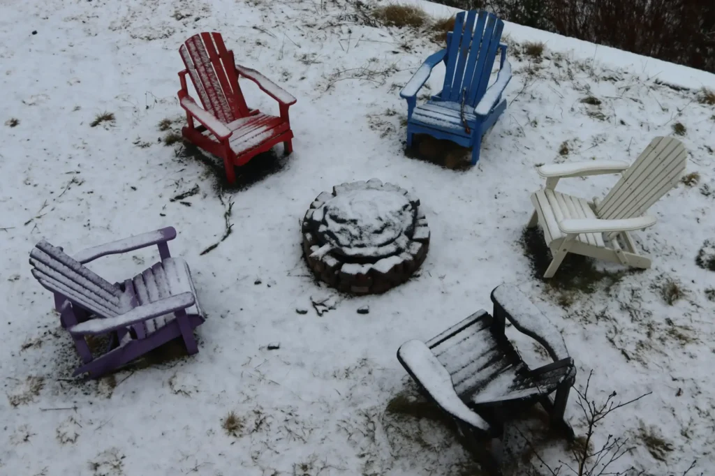 Outdoor chairs and a firepit covered in snow.